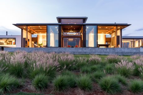 Sleek modern home with wood accents, expansive glass walls, and lush grass landscaping.