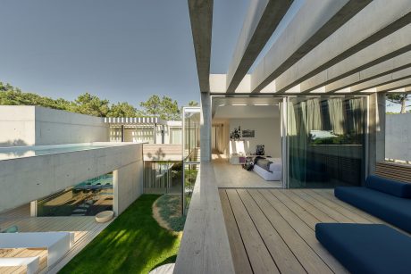 Modern architectural design with concrete beams, wooden deck, and landscaped indoor-outdoor space.