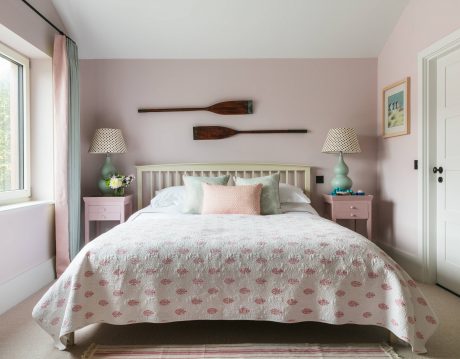 A cozy, pastel-colored bedroom with wooden oar wall decor and matching side tables.