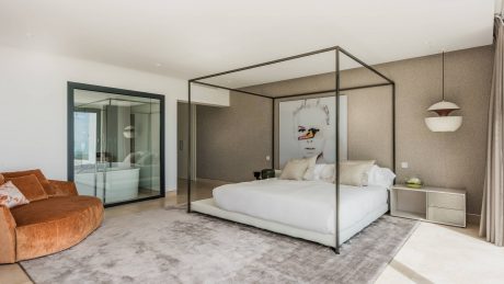 Sleek modern bedroom with a four-poster bed, glass walls, and an orange sofa.