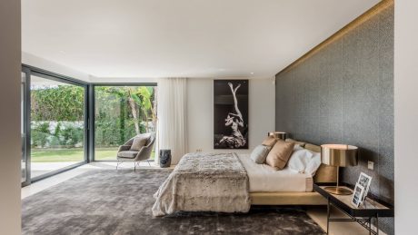 Luxurious modern bedroom with minimalist furnishings, sliding glass doors, and abstract artwork.