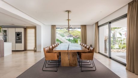 Spacious modern dining room with large wooden table, leather chairs, and garden views.