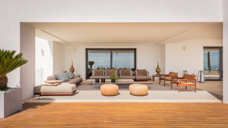 Spacious, modern living room with large sectional sofa, wooden deck, and floor-to-ceiling windows.