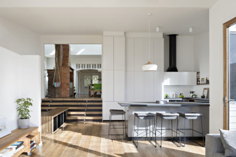 A modern kitchen with sleek cabinets, a striking brick wall, and an elevated dining area.