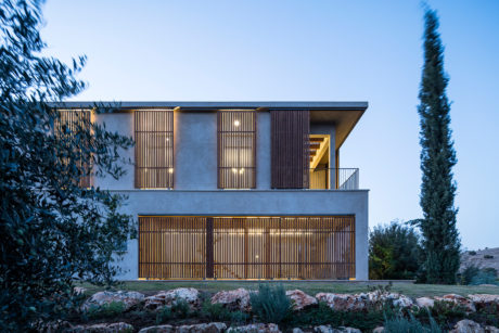 Two-story modern building with wooden slat panels and large windows surrounded by landscaping.