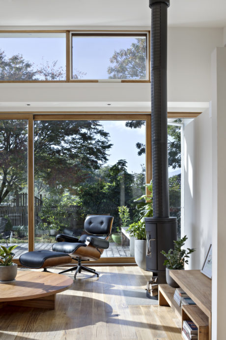 Expansive windows frame lush greenery, with a stylish lounge chair and wood accents.