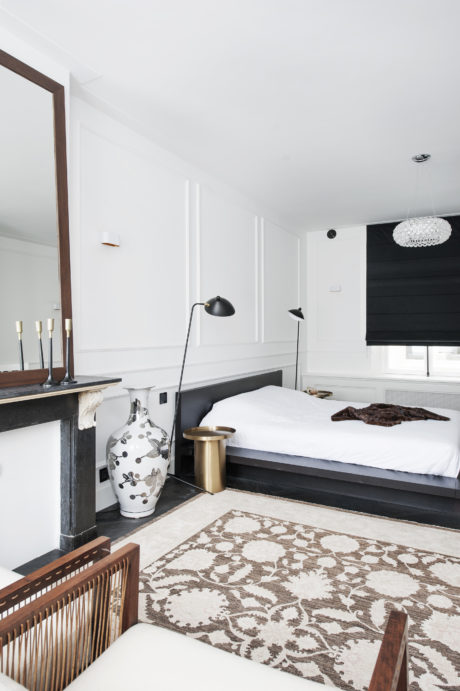 A modern, minimalist bedroom with elegant furniture, lighting, and a patterned area rug.