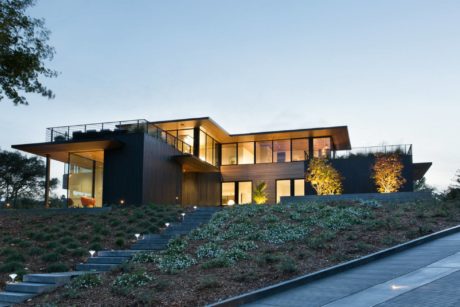 Sleek, modern architecture with wooden and glass elements, set on a hillside landscaped with plants.