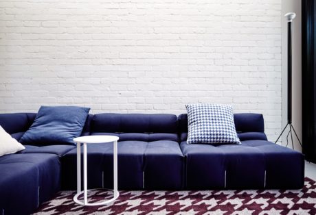 Minimalist living space with navy blue modular sofa, side table, and patterned rug.