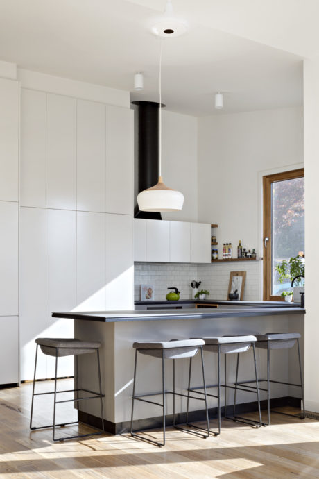Modern kitchen with sleek white cabinetry, pendant lighting, and metal bar stools.