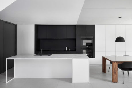 Monochrome modern kitchen with sleek black cabinets, white island, and minimalist lighting.