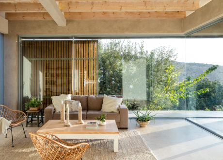 Warm, rustic living room with wood-beamed ceiling, glass walls, and modern furnishings.
