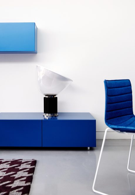 A modern, minimalist room with a blue cabinet, white lamp, and blue upholstered chair.
