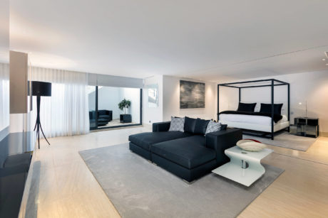 A spacious, modern bedroom with a large, plush black sofa and a sleek, four-poster bed.