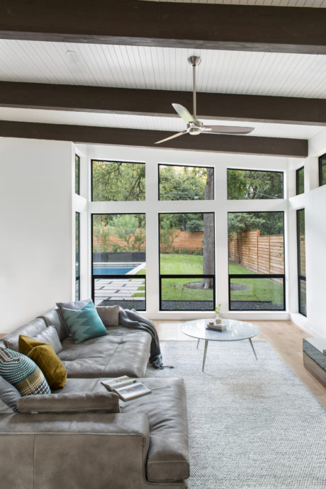 Spacious living room with large windows overlooking a lush backyard, sleek ceiling fan.