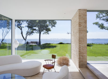 Expansive waterfront view through floor-to-ceiling glass, framed by brick accent wall.