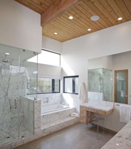 Spacious bathroom with wood-paneled ceiling, marble finishes, and glass shower enclosure.