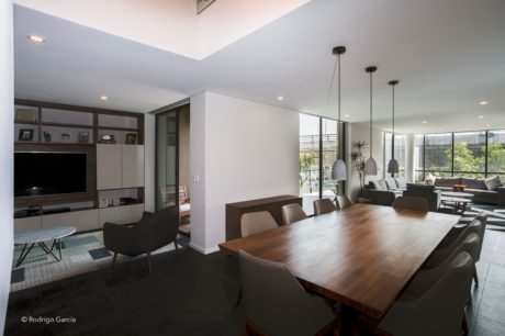 Modern, open-concept living space with wood dining table, pendant lights, and large windows.