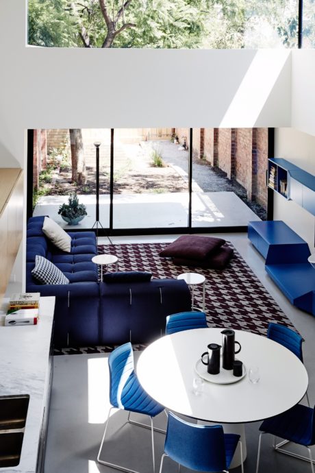 Modern living room with minimalist blue furniture, patterned rug, and large window overlooking a lush outdoor space.