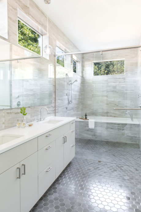 A modern, minimalist bathroom with a marble-tiled shower, hexagonal floor tiles, and large windows.