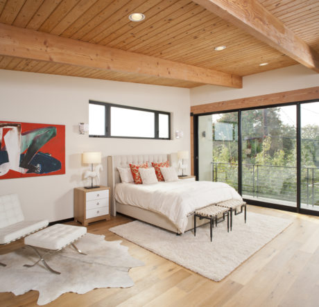 Cozy bedroom with wood-paneled ceiling, large windows, and modern furnishings.