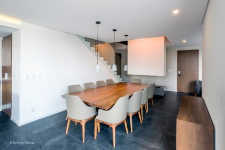 Spacious dining area with wooden table, plush chairs, and modern pendant lighting.