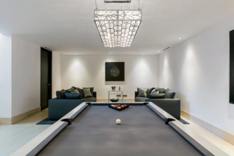 Sleek living room with modern pool table, elegant chandelier, and minimalist decor.