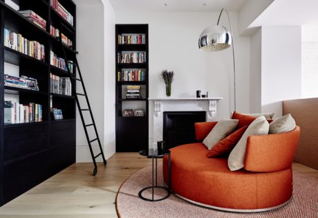 Cozy living room with large built-in bookshelves, a plush orange armchair, and a sleek chrome lamp.