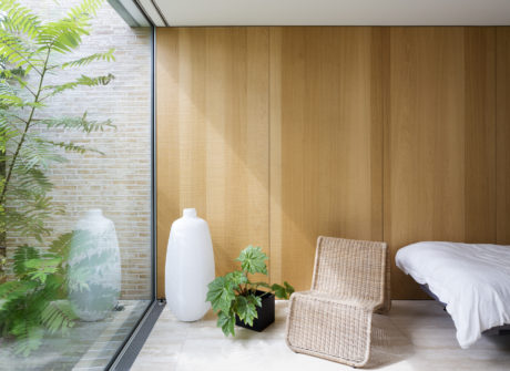 Wood-paneled bedroom with large window, potted plants, and woven armchair.