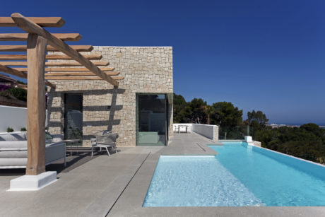 Contemporary Mediterranean villa with sleek stone exterior, pool, and covered patio.