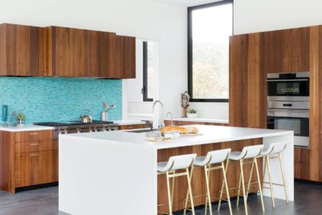 Modern kitchen with wooden cabinetry, white countertops, and turquoise tile backsplash. Large island with bar stools.
