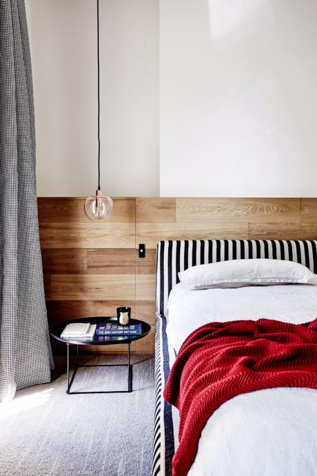 Cozy bedroom with wooden paneled walls, striped bedding, and sleek side table.