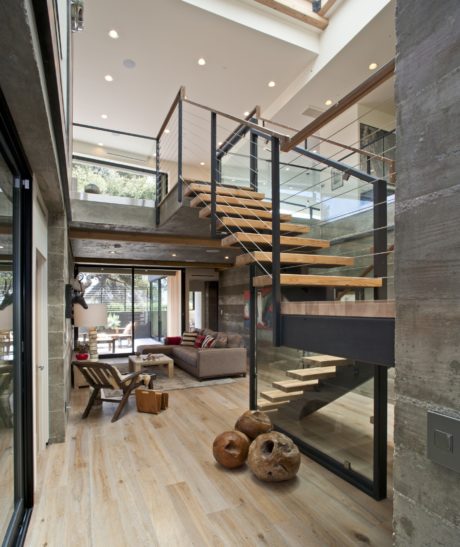 Modern open-plan interior with sleek staircase, glass walls, and rustic accents.