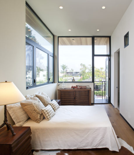 Spacious bedroom with tall windows, modern furniture, and a serene outdoor view.