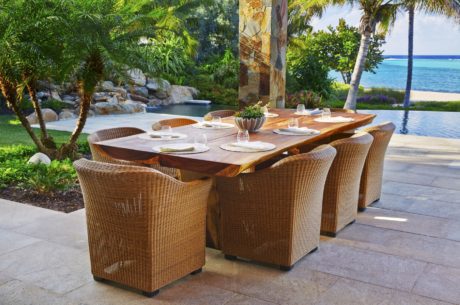 Luxurious outdoor dining area with wooden table, wicker chairs, and lush tropical surroundings.