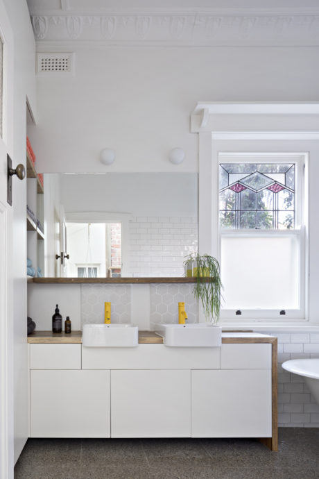A bright, modern bathroom with a white vanity, geometric window, and tile accents.