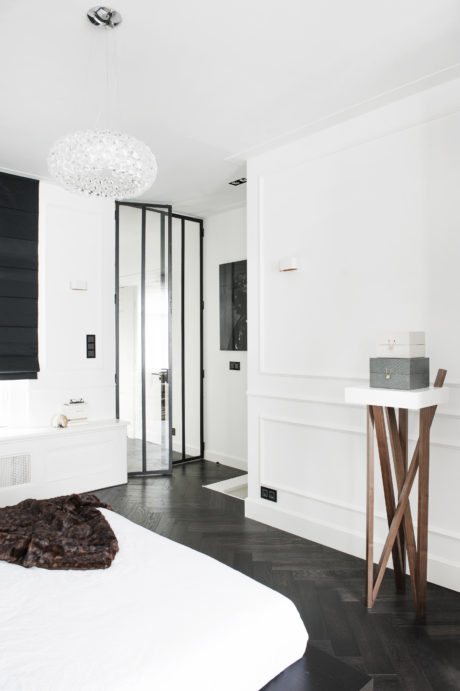 Minimalist bedroom with monochromatic decor, crystal chandelier, and modern furniture.