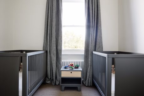 Cozy nursery with gray cribs, checkered curtains, and a side table with toys.