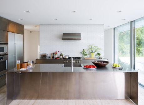 Sleek, modern kitchen with stainless steel countertops, white subway tiles, and large windows.