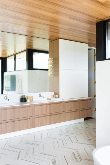 Modern, open-plan kitchen with wood-paneled walls, sleek white cabinets, and patterned tile floor.