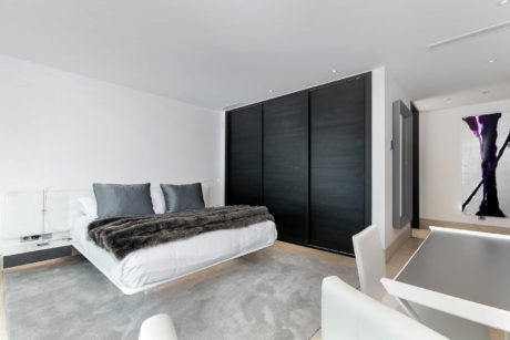 Minimalist bedroom with sleek black wardrobe, plush bedding, and modern lighting.