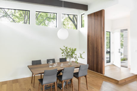 Minimalist dining room with wood accents, large windows overlooking greenery.