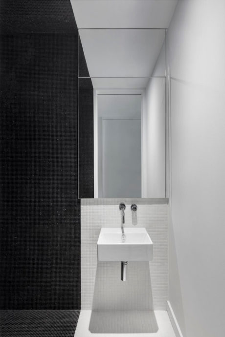 A minimalist bathroom with contrasting black and white tiles, a wall-mounted sink, and a mirrored cabinet.