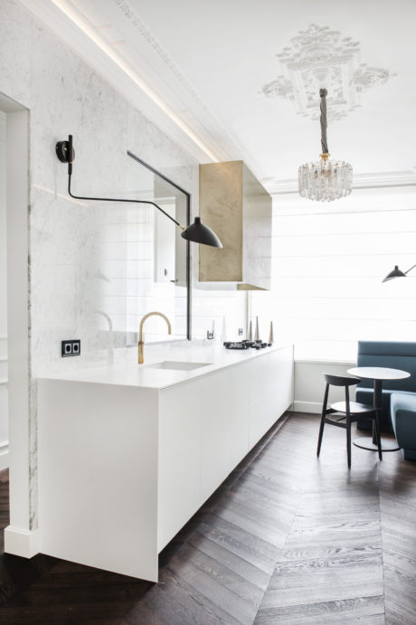 Sleek white kitchen with marble backsplash, contemporary lighting fixtures, and wood flooring.