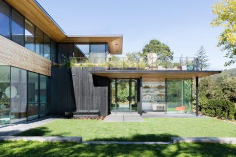 Modern wood-and-glass residence with expansive windows, exterior decking, and lush landscaping.
