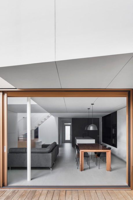 Modern, minimalist living area with dark furniture and wooden dining table framed by large glass windows.