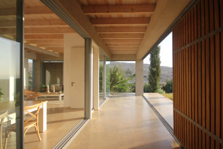 Spacious covered patio with wooden beams, glass doors, and views of the surrounding landscape.