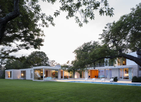 Sleek modern home with floor-to-ceiling windows, a pool, and lush surrounding trees.