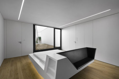 Modern interior with minimalist design, featuring sleek white walls, a black built-in couch, and large windows overlooking an outdoor deck.