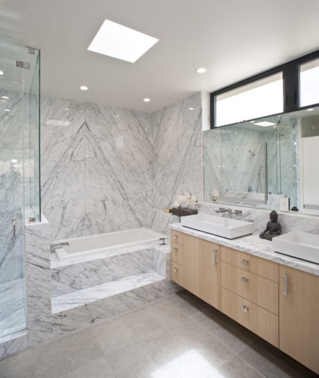 A modern, sleek bathroom with marble walls, a large tub, and a wooden vanity.